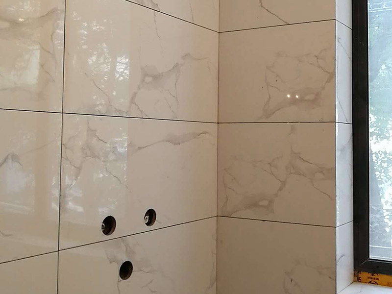 衛(wèi)生間瓷磚鋪貼：基層處理：首先應除去基層表面的污垢，油漬，浮灰;除去基層上所有涂料層，膩子層;如果基層未能達到平整度要求，需對基層進行預先的找平處理。  放樣：鋪貼瓷磚前需事先找好垂直線，以此為基準鋪貼的瓷磚高低均勻、垂直美觀;此外，施工前在墻體四周需彈出標高控制線，在地面彈出十字線，以控制地磚分隔尺寸。  預鋪：首先應對瓷磚的色彩、紋理、表面平整等進行嚴格的挑選，然后按照圖紙要求預鋪。 調制粘結劑：加水后將粘結劑漿料攪拌至潤滑均勻，無明顯塊狀或糊狀結塊，攪拌后的漿料靜置5-10分鐘后再稍加攪拌1-2分鐘即可使用。在開始鋪貼施工前，需要先清理瓷磚表面的浮灰，污垢等。  抹漿料：將調制好的漿料均勻地抹在瓷磚背面，要求漿料飽滿。將瓷磚平整地鋪貼在基層上，使用橡膠錘將瓷磚拍實鋪平。施工過程中，可小幅度轉動瓷磚，使?jié){料與瓷磚背面充分接觸。 瓷磚鋪貼結束后24小時，可進行嵌縫施工。將調制好的嵌縫劑均勻地涂在磚與磚的縫隙內(nèi)。嵌縫后用浸濕的織物清理多余的嵌縫劑，保持瓷磚表面清潔。