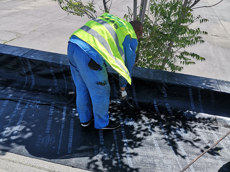 屋頂防水卷材鋪貼:清除基層表面雜物、油污、砂子，凸出表面的石子、砂漿疙瘩等應(yīng)清理干凈，清掃工作必須在施工中隨時(shí)進(jìn)行，并修補(bǔ)平整表面。尤其鏟除排水口、煙囪、管壁上的水泥砂漿等附著物；根據(jù)施工現(xiàn)場(chǎng)狀況，進(jìn)行合理定位，確定卷材鋪貼方向，在基層上彈好卷材控制線，依循流水方向從低往高進(jìn)行卷材試鋪。卷材試鋪后，先將要鋪貼的卷材剪好，反鋪于基面上(即是底部隔離紙朝上)，撕剝?nèi)ゾ聿母綦x紙。撕剝時(shí)，已剝開的隔離紙宜與粘結(jié)面保持45～60度的銳角，防止拉斷隔離紙，盡量保持在自然松弛狀態(tài)，但不要有皺折。