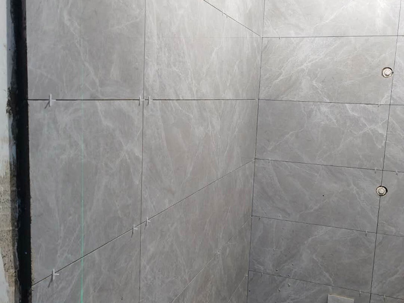 衛(wèi)生間貼磚施工：應全部清理墻面上的各類污物，打掃干凈現(xiàn)場，特別是腳落里。用泥刀先批墻，后用水泥漿找平。這個工序很重要，確保底子平，防止貼后空鼓。墻面要刷防水涂料，防止貼后浸水，一般高度不低于1.8米，刷的時候會稍高一些。根據(jù)設計鋪貼圖樣的要求，確定排磚方案，用墨斗彈線，以減少施工損耗。把剛剛攪拌好的粘結(jié)劑漿料均勻的刮到墻上。瓷磚上墻將經(jīng)過預先清潔的瓷磚平整地鋪貼在粘結(jié)劑漿料基層上，使用橡膠錘將瓷磚拍實鋪平。施工過程中，可小幅度轉(zhuǎn)動瓷磚，使?jié){料與瓷磚背面充分接觸。專家建議在鋪貼時，隨機取下已鋪貼于基層上的瓷磚作檢查。確保漿料與瓷磚背面的充分接觸。 留縫大小調(diào)整根據(jù)瓷磚的尺寸，在磚與磚之間預留相應尺寸的縫隙留待嵌縫?？捎醚篮灥认裙潭ǎ辰Y(jié)劑具有一定的可調(diào)整性，可對留縫的大小進行調(diào)整。