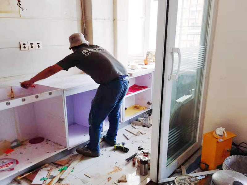 廚房櫥柜安裝：清理：對廚房作防護(hù)措施，掛擋布、廚房墻面等做簡單清理，以便準(zhǔn)確測量地面水平。櫥柜安裝一般先從地柜開始。把櫥柜外包裝拆開后。在櫥柜的邊緣貼上防火膜封邊。在下柜底部安裝上支腳，根據(jù)地面水平高度調(diào)整櫥柜。 櫥柜安裝需要找出基準(zhǔn)點，L型廚房從直角處向兩邊延伸，U型廚房則先將中間的一字型柜體放整齊后，再從兩個直角處向兩邊站看，這樣可以避免出現(xiàn)縫隙。櫥柜框架安裝牢固定位后，需要在櫥柜背面安裝背板。一般安裝下水都會現(xiàn)場開孔，工人會用專業(yè)的打孔器按照管道大小進(jìn)行打孔，打孔的直徑應(yīng)比管道大3-4毫米，并且打孔后要將開孔部分用密封條封邊，防止邊緣滲水木材變形。